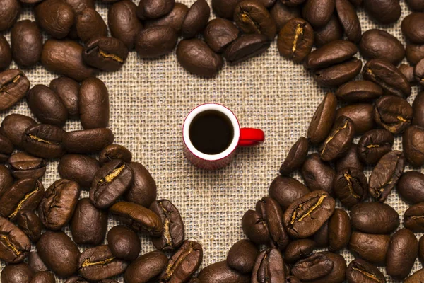 Corazón de granos de café y una taza sobre fondo de arpillera —  Fotos de Stock