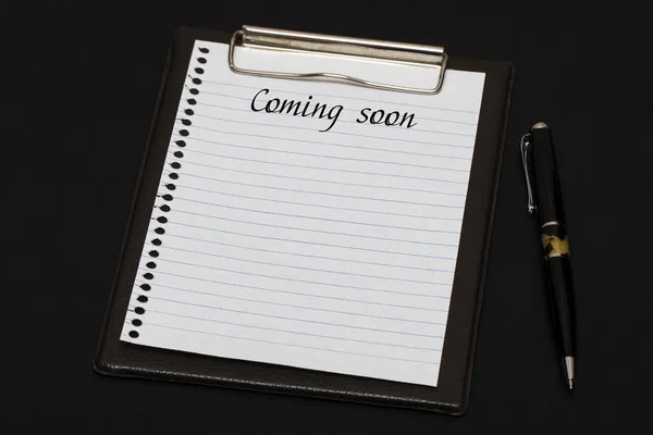 Top view of clipboard and white sheet written with Coming soon o — Stock Photo, Image