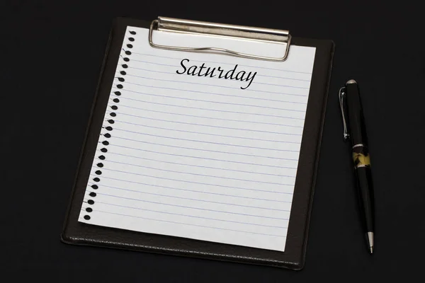 Top view of clipboard and white sheet written with Saturday on b — Stock Photo, Image