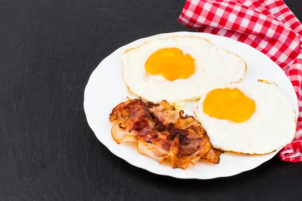 Desayuno con huevos fritos y tocino sobre fondo de piedra oscura — Foto de Stock