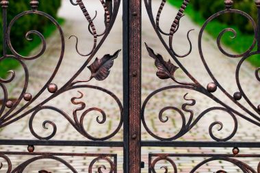 A closed forged metal gate looking onto a garden path clipart