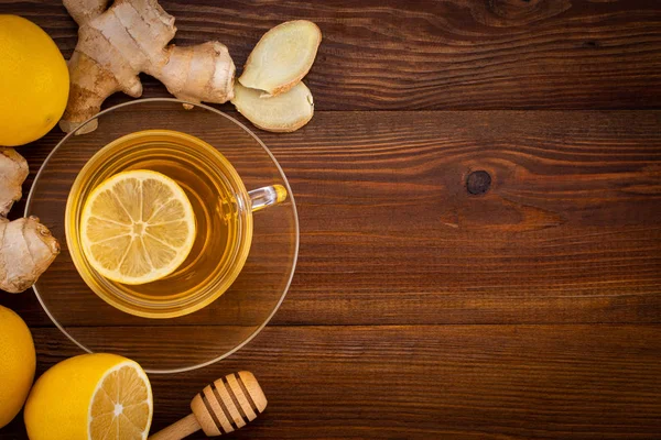 Cup of Ginger tea with lemon, honey and ginger root on a wooden