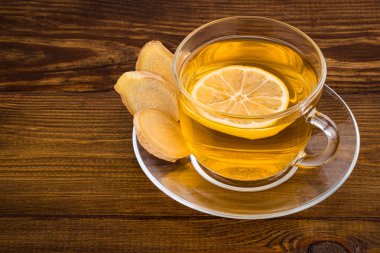 Bir bardak limonlu zencefil çayı ve ahşap bir sırtta zencefil kökü.