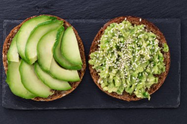 Avokado sandviçi koyu arkaplanda koyu çavdar ekmeği, üst manzara..