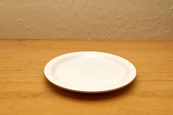 Пустая белая тарелка на деревянном столике напротив стены — стоковое фото