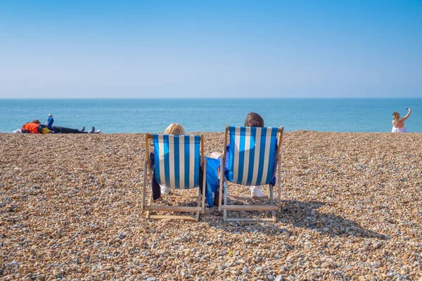 Paar sitzt in Liegestühlen am Strand. lizenzfreie Stockbilder