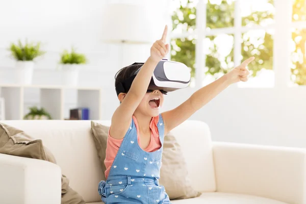 En glad liten jente med virtual reality hodetelefoner sittende på sofaen – stockfoto