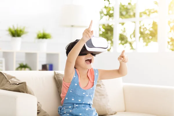 En glad liten jente med virtual reality hodetelefoner sittende på sofaen – stockfoto
