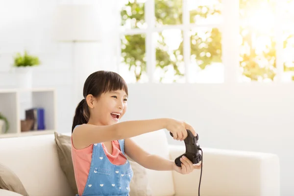 Смеющаяся маленькая девочка играет в видеоигры на диване — стоковое фото