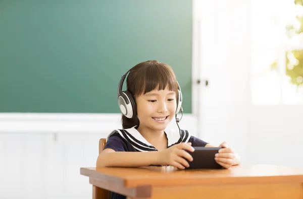 Menina feliz aprendendo com telefone inteligente em sala de aula — Fotografia de Stock