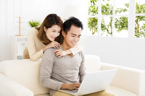 Happy young couple using laptop on sofa — Stockfoto