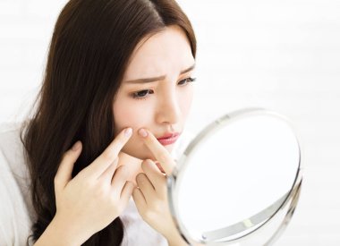 young woman squeeze her acne in front of the mirror clipart