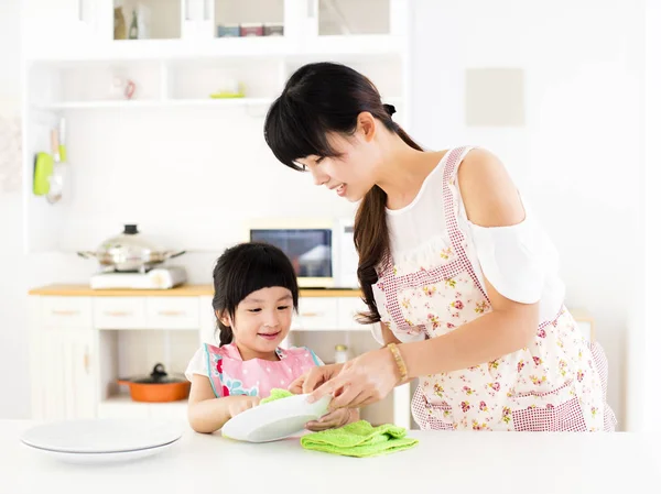 Niña ayudando a su madre a limpiar el plato en la cocina —  Fotos de Stock
