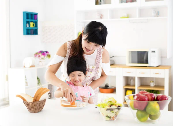 Маленькая девочка помогает матери готовить еду на кухне — стоковое фото