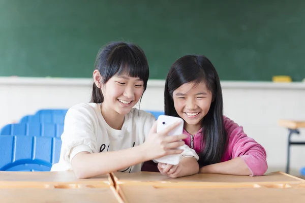 Twee tienermeisjes student kijken de telefoon in de klas — Stockfoto