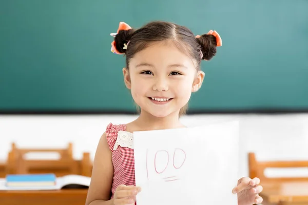 Lycklig liten flicka visar tentamen med ett plus i klassrummet — Stockfoto