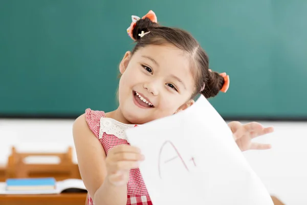 Niña feliz mostrando papel de examen con un plus en el aula —  Fotos de Stock