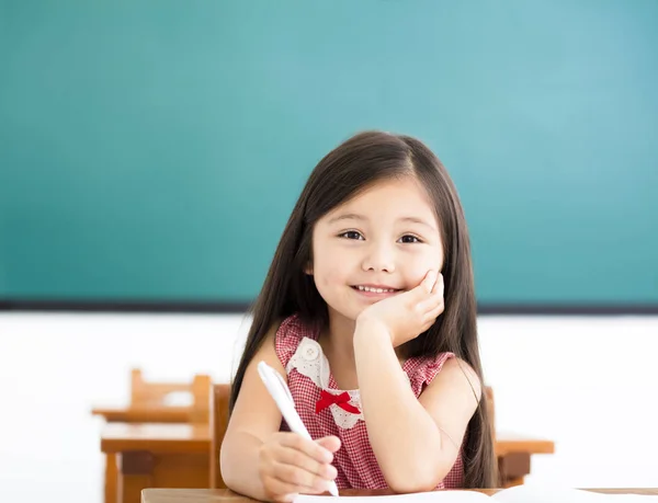 Menina feliz escrevendo na mesa em sala de aula — Fotografia de Stock