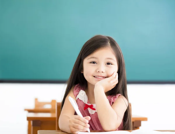 Niña feliz escribiendo en el escritorio en el aula —  Fotos de Stock