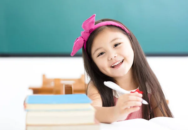 Menina feliz escrevendo na mesa em sala de aula — Fotografia de Stock