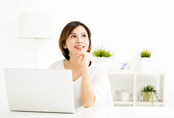 Junge Frau mit Laptop und Denken im Wohnzimmer — Stockfoto