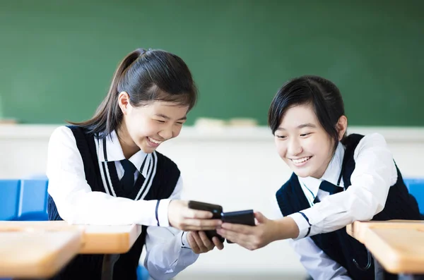 Niñas estudiantes felices viendo el teléfono inteligente en el aula —  Fotos de Stock