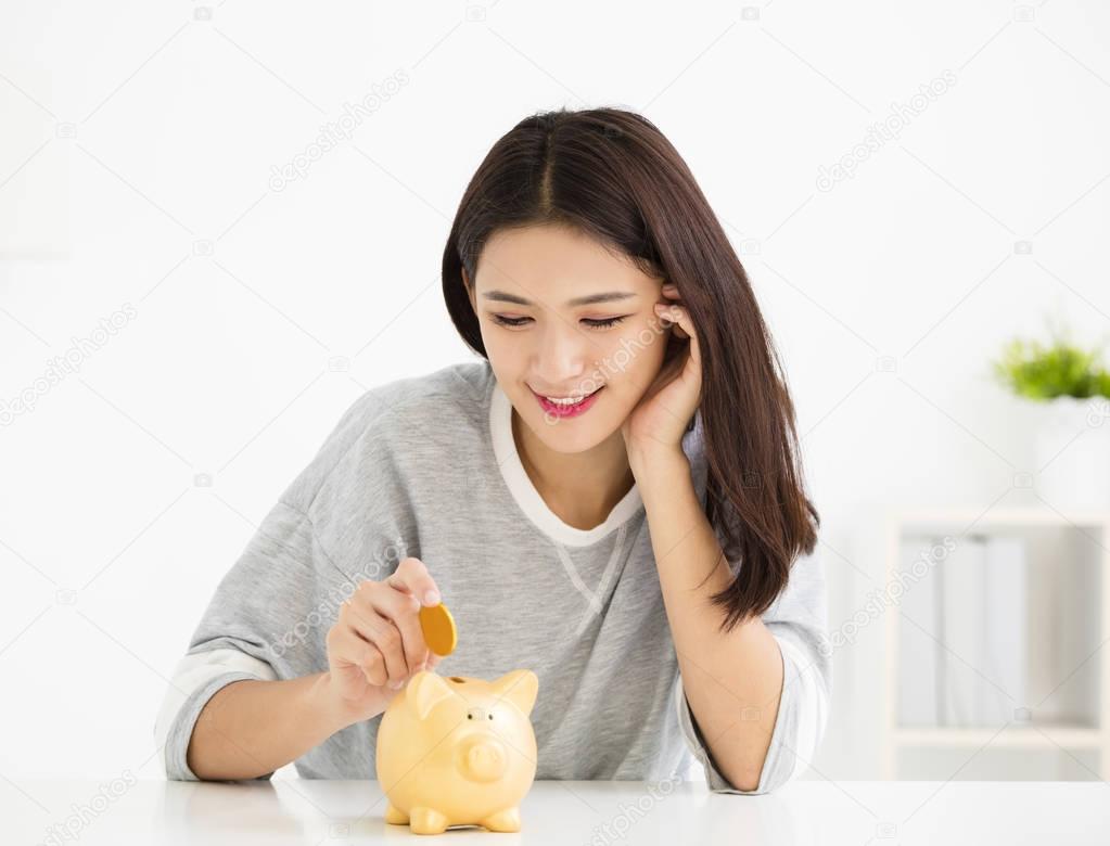 smiling young Woman Putting Coin In Piggy Bank