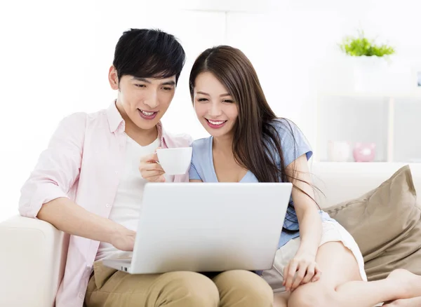 Feliz jovem casal sentado no sofá com laptop — Fotografia de Stock