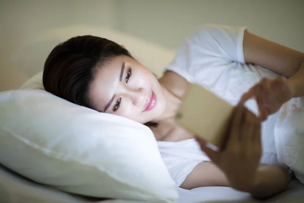 Jonge vrouw kijken slimme telefoon in bed bij nacht — Stockfoto