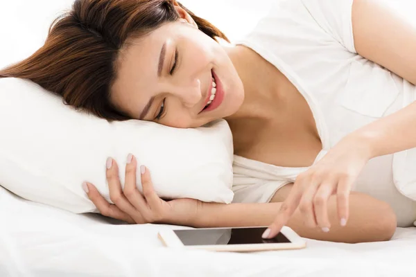 Mladá žena sleduje chytrý telefon v posteli — Stock fotografie