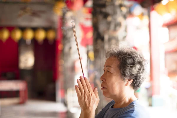 Mulher sênior orando buddha com pau de incenso no templo — Fotografia de Stock