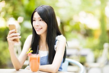 gülümseyen genç kadın akıllı telefon izlerken restoranda oturan