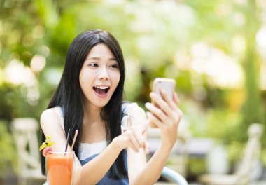 akıllı telefon izlerken restoranda oturan sürpriz genç kadın