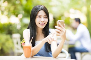 gülümseyen genç kadın akıllı telefon izlerken restoranda oturan