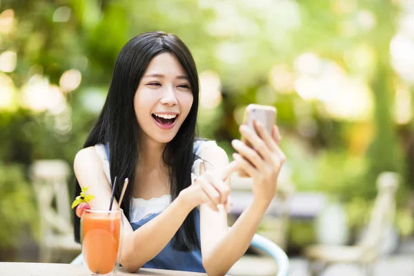 Улыбающаяся молодая женщина сидит в ресторане и смотрит смартфон — стоковое фото