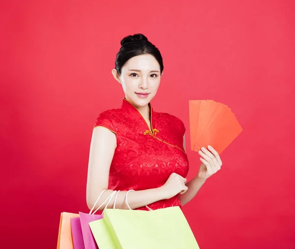 Mujer sonriente mostrando el sobre rojo y bolsas de compras — Foto de Stock