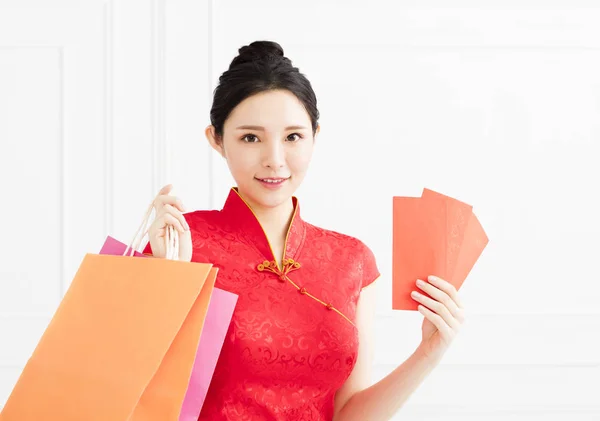 Mujer sonriente mostrando el sobre rojo y bolsas de compras — Foto de Stock