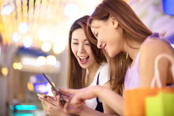 Счастливые девушки смотрят телефон в торговом центре — стоковое фото