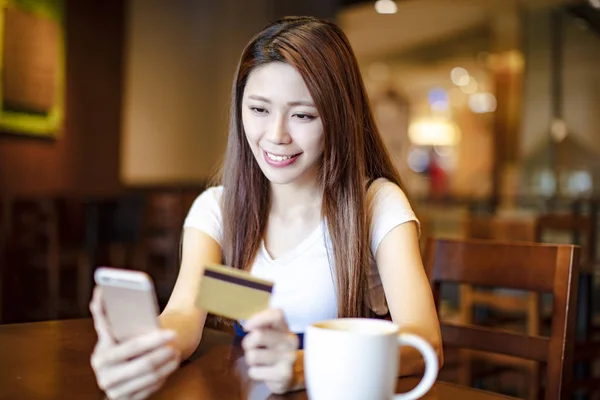 Woman holding credit card and smart phone in coffee shop — Stock Photo, Image