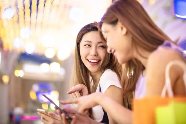 Glada tjejer titta på telefonen i köpcentrum — Stockfoto