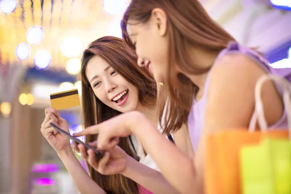 Meninas mostrando cartão de crédito e assistindo telefone no shopping mal — Fotografia de Stock