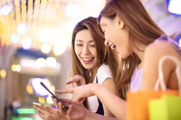 Meninas felizes usando telefone inteligente no shopping — Fotografia de Stock