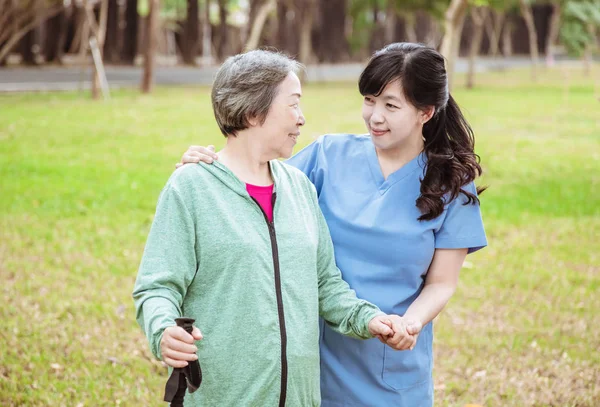 Улыбающаяся медсестра помогает пожилой женщине гулять по парку — стоковое фото