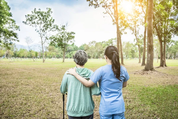 Krankenschwester hilft Seniorin beim Spaziergang durch den Park — Stockfoto