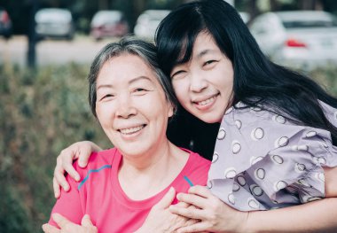 Asyalı kıdemli anne ve yetişkin kızı birbirlerine sarılıyorlar.