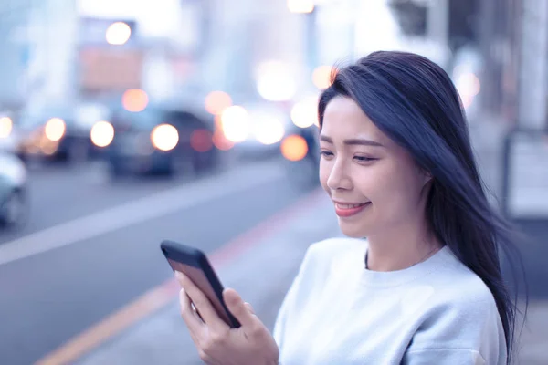 Ung kvinna tittar på smart telefon i staden på natten — Stockfoto