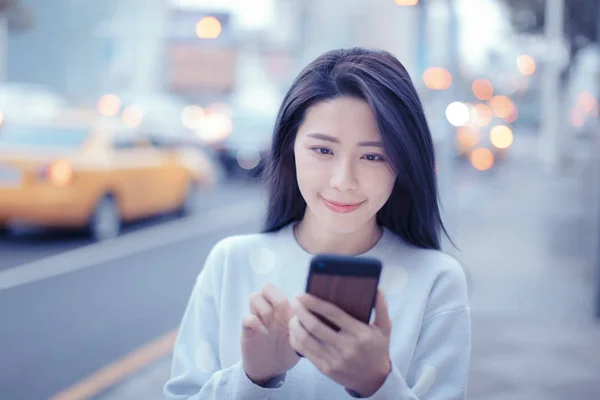 Ung kvinna tittar på smart telefon i staden på natten — Stockfoto