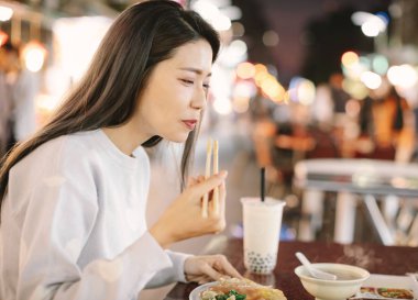 Night Mar 'da Asyalı kadın sokak yemeğiyle köpüklü sütlü çayın keyfini çıkarıyor