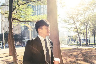 İş adamı elinde cep telefonu tutarken caddeden ofise yürüyor.