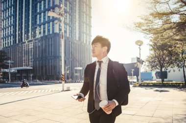 İş adamı elinde cep telefonu tutarken caddeden ofise yürüyor.